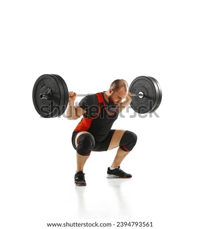 Muscular, strong young athlete, bodybuilder doing squats and lifting barbell, heavy weights over white background. Concept of sport, strength, gym, healthy lifestyle, power, endurance, weightlifting