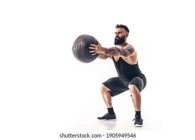 Muscular tattooed bearded male exercising fitness weights Medicine Ball in studio isolated on white background.