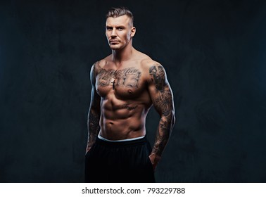 A muscular tattooed man on a dark background.