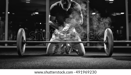 Muscular weightlifter clapping hands and preparing for workout at a gym.