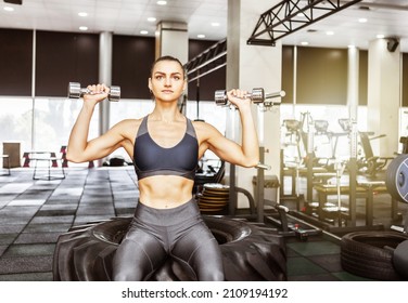 Muscular Woman Training Shoulders Doing Dumbbell Press Sitting On Cross Wheel In A Modern Gym