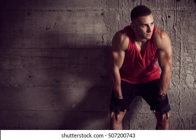 Muscular young athletic built sportsman, leaning against a concrete wall of an abandoned building, taking a break