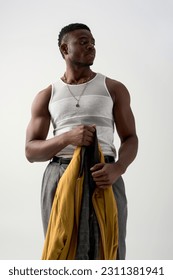 Muscular young black man in tank top and pants holding trendy bomber jacket isolated on grey, contemporary shoot featuring stylish attire, fashion statement