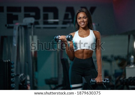 Muscular young fitness sports woman workout with dumbbells in fitness gym.
