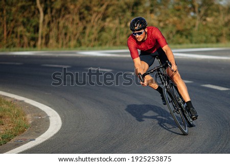 Muscular young guy wearing sport clothing, protective helmet and mirrored glasses enjoying sport activity on black bike. High speed and racing.