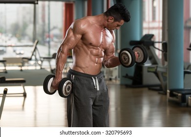 Muscular Young Man Doing Heavy Weight Exercise For Biceps With Dumbbells In Modern Fitness Center