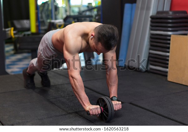 Muscular young man performing exercises with the\
abdominal wheel. inside the\
gym
