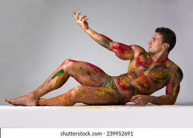 Muscular young man shirtless with skin painted with Holi colors, laying down on the floor striking a pose