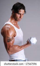 Muscular Young Man Standing In Jeans And A White Wife Beater Tee Shirt Working Out Lifting Weights