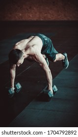 Muscular Young Man Training Burpee With Dumbbells On The Gym Floor