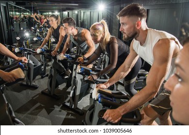 Muscular Young Men And Women On Cycling Class At Gym.