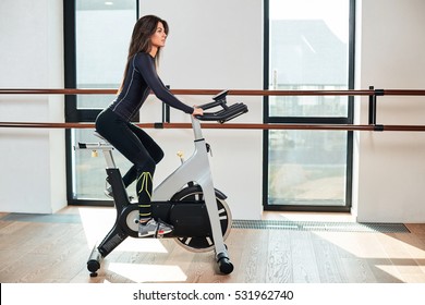 Muscular Young Woman Working Out On The Exercise Bike At The Gym, Intense Cardio Workout.