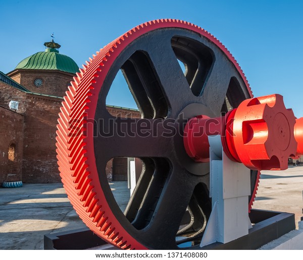 Museum exhibit: gear wheel on the background of an\
old brick tower