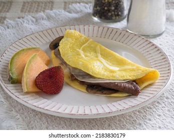 Mushroom Omelette Stuffed With Melted Cheese And Sliced Beefsteak, Accompanied By Slices Of Fresh Cantaloupe And Strawberry