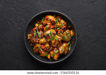 Mushrooms Manchurian dry in black bowl at dark slate background. Mushroom Manchurian - is indo chinese cuisine dish with deep fried mushrooms, bell peppers, sauce and onion.