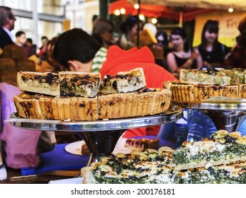 Mushrooms, spinach and broccoli pies on display at pastry stall in colorful food market - a famous Borough Market (London, England). People buying food at backgrounds. Selective focus.