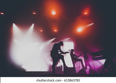 Music Band / Group With Guitar Player / Guitarist Silhouette Perform On A Concert Stage.  Dark Background, Smoke, Concert  Spotlights