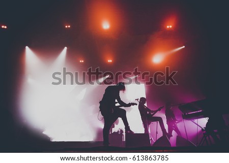 Music band / group with guitar player / guitarist silhouette perform on a concert stage.  Dark background, smoke, concert  spotlights
