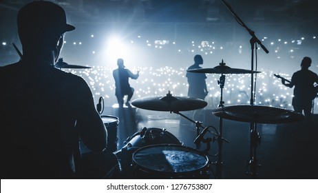 Music band group silhouette perform on a concert stage.  
silhouette of drummer playing on drums
audience holding cigarette lighters and mobile phones