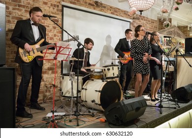 Music band of six young people (two women, four men) performs on stage in club