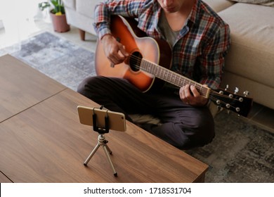 Music College Hipster Student Practicing Acoustic Guitar Exercise, Reading Notes From Phone On Tripod. Man Taking An Online Musical Courses At Home During Quarantine. Background, Close Up