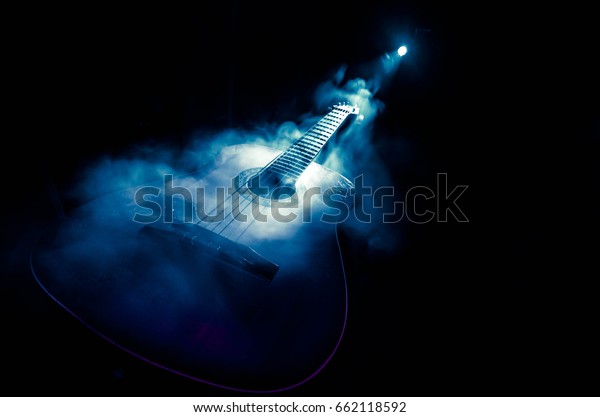 Music\
concept. Acoustic guitar isolated on a dark background under beam\
of light with smoke with copy space. Guitar Strings, close up.\
Selective focus. Fire effects. Surreal\
guitar