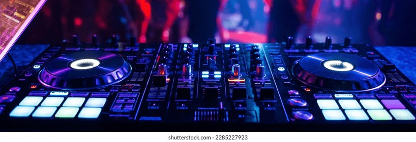 music controller DJ mixer in a nightclub at a party against the background of blurred silhouettes of dancing people