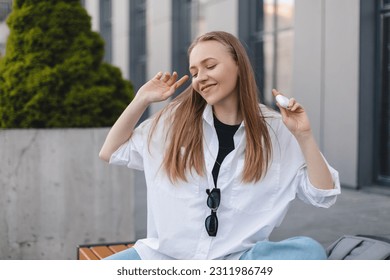 Music, dance and motivation with a business woman walking near office while feeling positive or carefree. Success, happy or smile with woman employee sitting near work in headphones with a smile. Win. - Shutterstock ID 2311986749