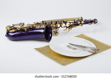 Music And Dinner - Violet Saxophone With A Porcelain Plate, Fork, Knife And Golden Food Pad On White Background