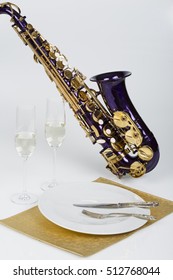 Music And Dinner - Violet Saxophone With Two Glasses Of White Wine, A Porcelain Plate, Fork, Knife And Golden Food Pad On White Background