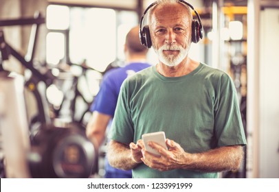 With Music Exercises Are Easier. Senior Man At Gym Listening Music On Smart Phone. Close Up.