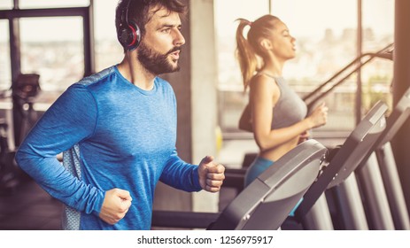 Music and exercises go together. Couple working exercise on treadmill. Focus is on man.  - Shutterstock ID 1256975917