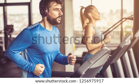 Music and exercises go together. Couple working exercise on treadmill. Focus is on man. 