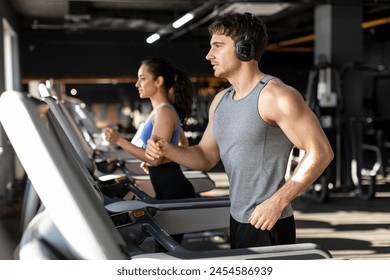 Music and exercises go together. Fit man and woman exercising on treadmill, enjoying morning workout - Powered by Shutterstock