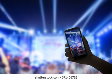 Music fans takes smartphone video records at concert.