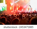 Music festival atmosphere with vibrant stage lights, enthusiastic audience enjoying live performance, fans capturing moments on smartphones, friends celebrating together in open-air venue at dusk.