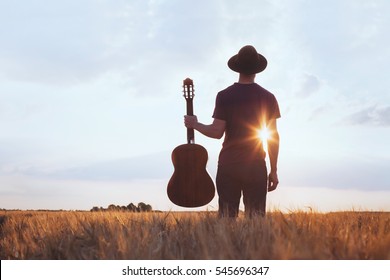 music festival background, silhouette of musician artist with acoustic guitar at sunset field
				