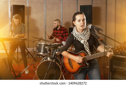 Music Garage Band With Passionate Emotional Woman Vocalist And Guitarist Practicing In Rehearsal Room