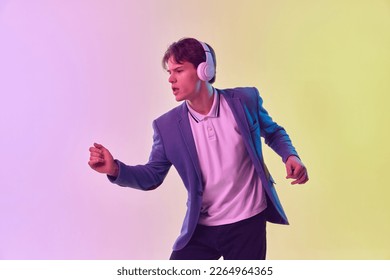 Music  Half  length portrait young man in headphones dancing isolated gradient yellow  purple background in neon light  Concept human emotions  youth culture  Copy space for ad 