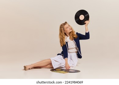 Music. Happy beautiful stylish young blonde woman with retro style hairdo wearing vintage outfit sitting on floor with vinyl record isolated over grey background. Beauty, ad, emotions - Shutterstock ID 2241984069