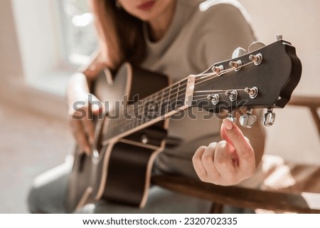 Music and hobbies. A talented young female musician is sitting alone and tuning a guitar. The lady plays a calm melody on a musical instrument.