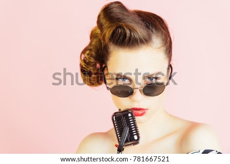 Music, look and retro style, pinup. Pin up young girl on pink background, radio. Woman singer with stylish retro hair and makeup. Beauty and vintage fashion. Girl in glasses sing in microphone.
