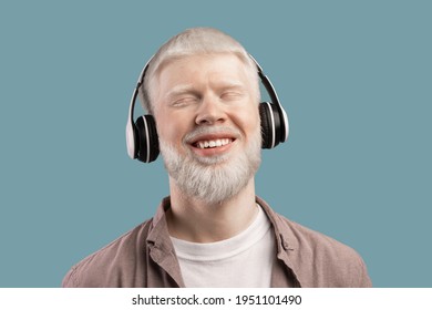 Music lover. Peaceful albino man in wireless headphones listening audio on turquoise studio background. Guy closing eyes and smiling, enjoying favourite melodies with pleasure - Powered by Shutterstock