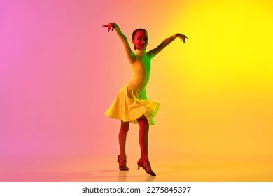 Music in movements  Emotional little girl in yellow stage dress dancing classical ballroom dance over gradient pink  yellow background in neon light filter  Concept beauty  professional dances