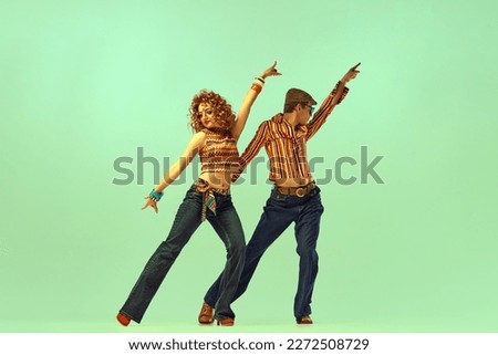 Music and moves. Two excited people, man and woman in retro style clothes dancing disco dance over green background. 1970s, 1980s fashion, vintage, hippie lifestyle