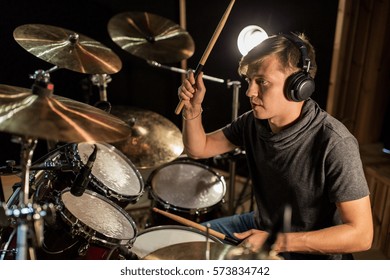 music, people, musical instruments and entertainment concept - male musician in headphones with drumsticks playing drums and cymbals at concert or studio - Powered by Shutterstock