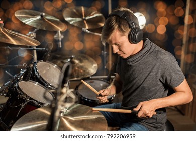 music, people, musical instruments and entertainment concept - male musician or drummer in headphones with drumsticks playing drums and cymbals at concert or studio over holidays lights background