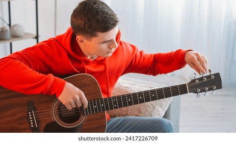 Music practice. Guitar adjusting. Talented performer. Concentrated young man artist tuning pegs and gears on string acoustic instrument at home. - Powered by Shutterstock