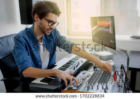 music producer is composing a song on synthesizer keyboard and computer in recording studio. Man is working on sound mixer in recording studio or DJ is working in broadcasting studio