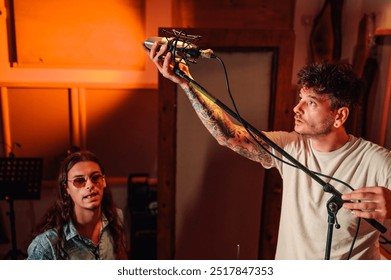 Music producer and sound engineer adjusting microphone in a soundproof booth with a young musician sitting nearby while working in a music studio. Copy space. - Powered by Shutterstock